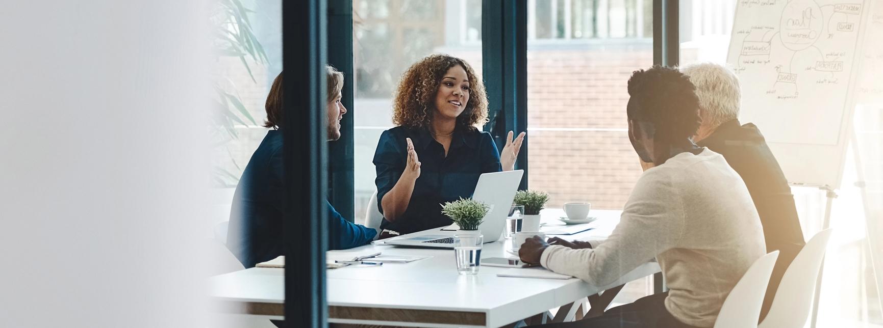 Group of business professionals sitting at a white boardroom table and talking. 