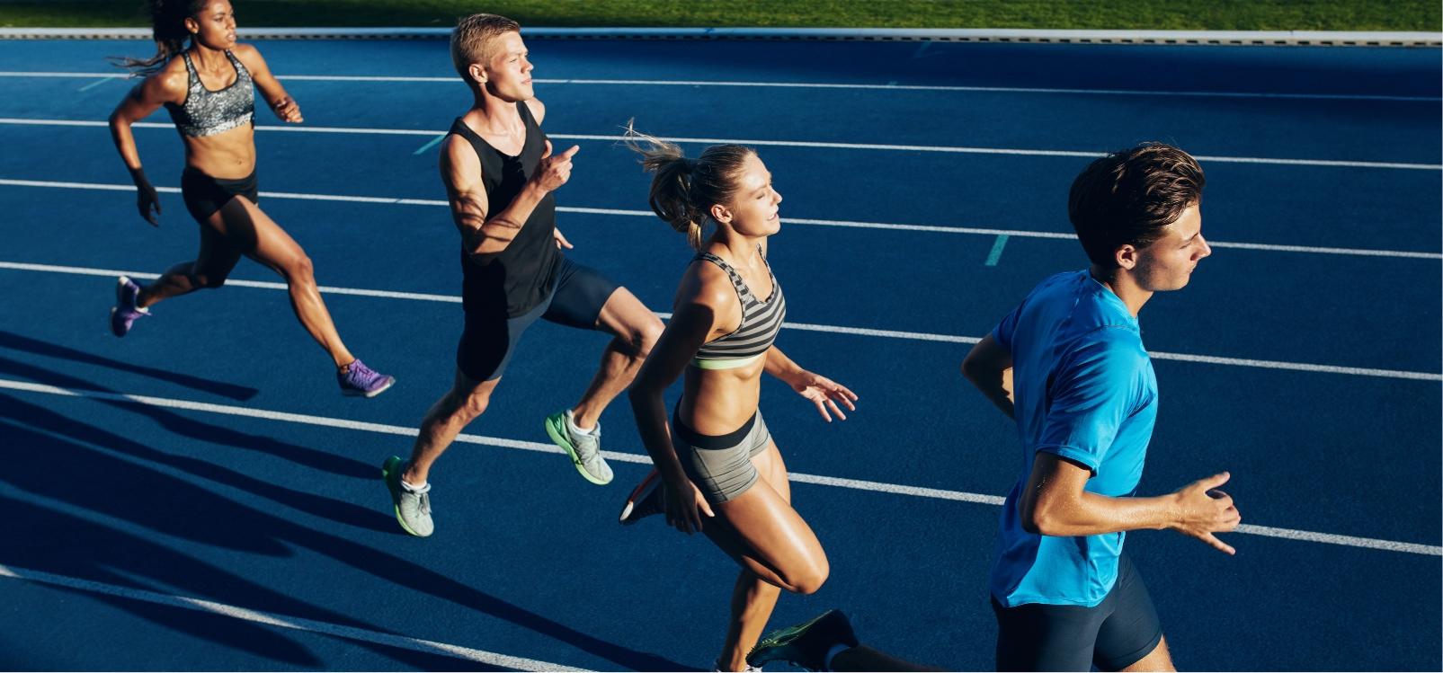 Group of four athletes sprinting on a blue track, focusing on their race.