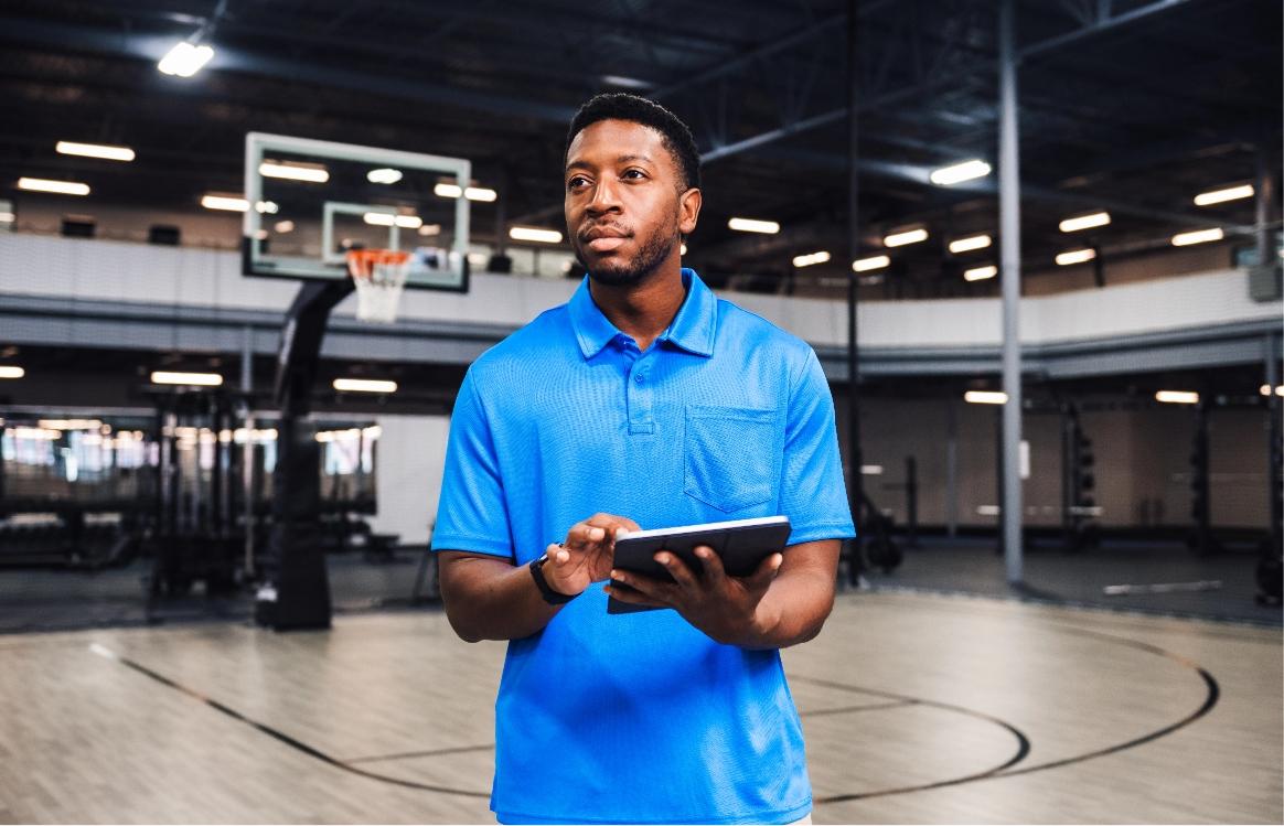 Gym owner holding a tablet overseeing everything within their indoor basketball court.