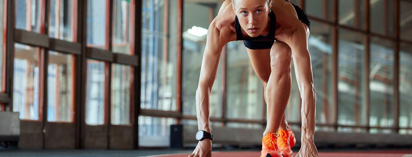 Female athlete in starting position on indoor track, focused and ready to sprint.