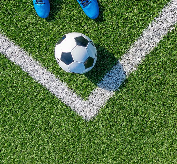 Soccer ball on artificial turf near the corner of the field with shoes in foreground