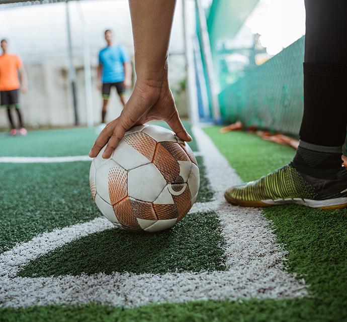 Close up of player setting a soccer ball on the turf field, ready to kick, teammates in the background.