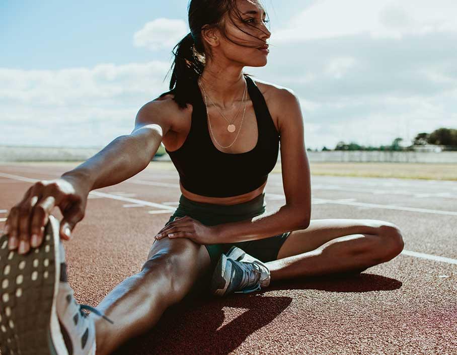 Female runner on an outdoor running track stretching her legs before her run.