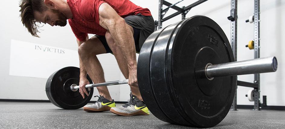 Man performing a deadlift in a gym with a barbell, focusing intently on his lift.