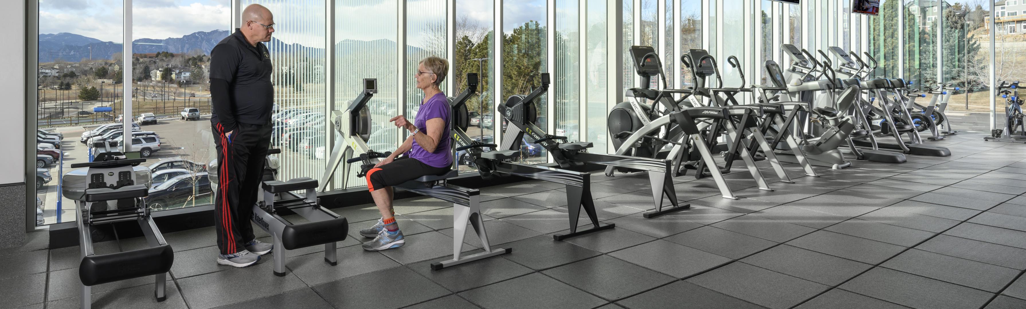 a woman and a man talking in a rec center on cardio equipment