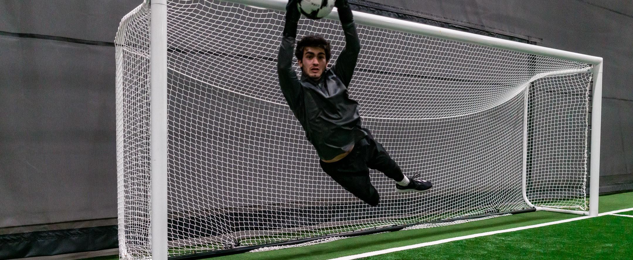 Goalie leaping to make a save on an indoor soccer field.