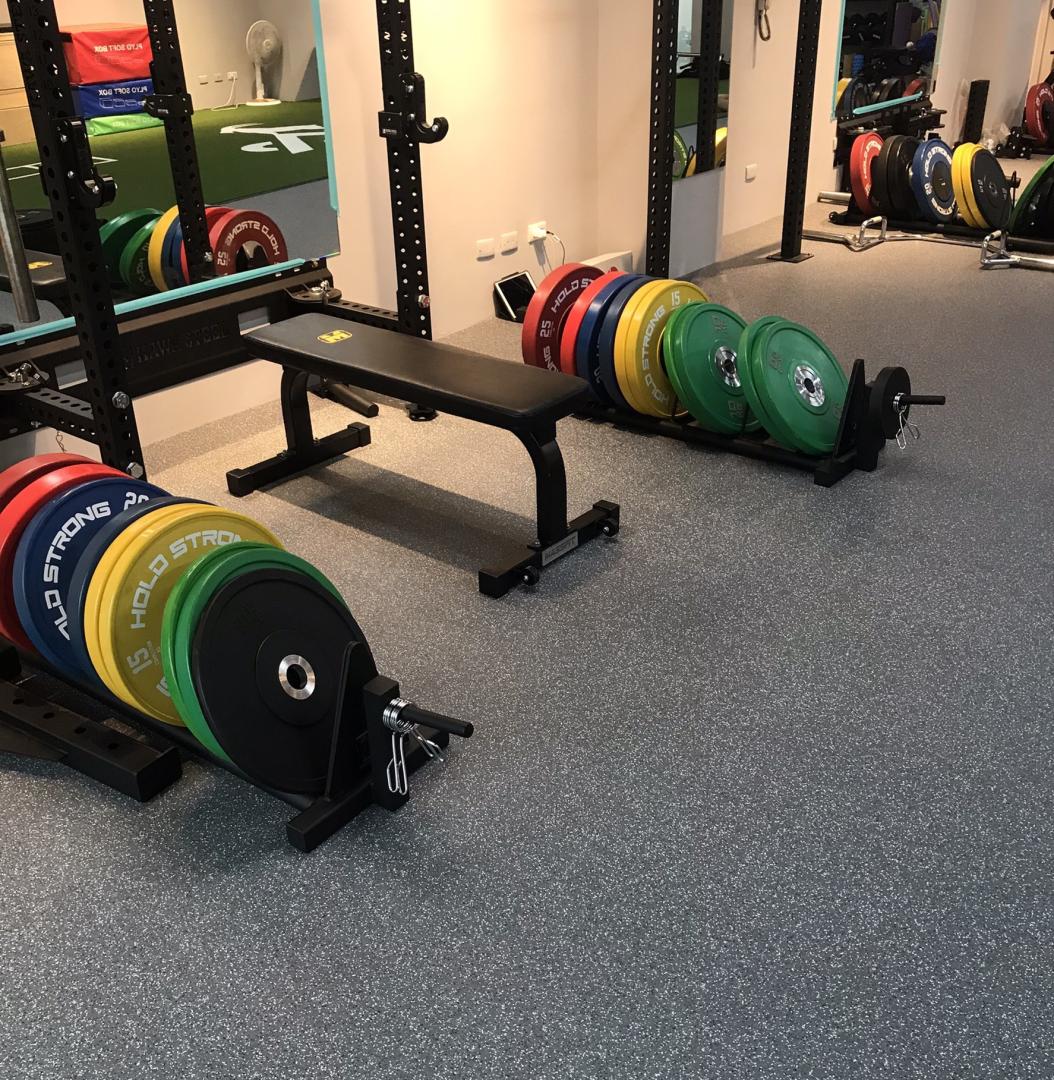 Interior of a gym showcasing weights and benches for strength training exercises on top of ComPact-Fleck flooring.