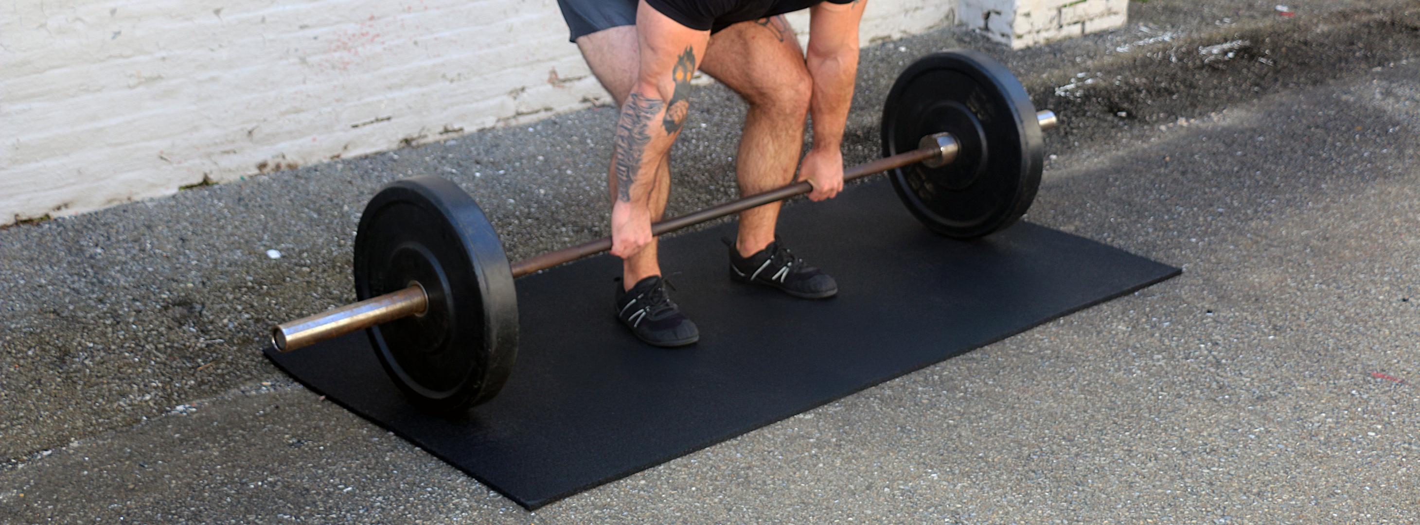 A man lifts a barbell while standing on a smash mat, focusing on his strength training exercise.