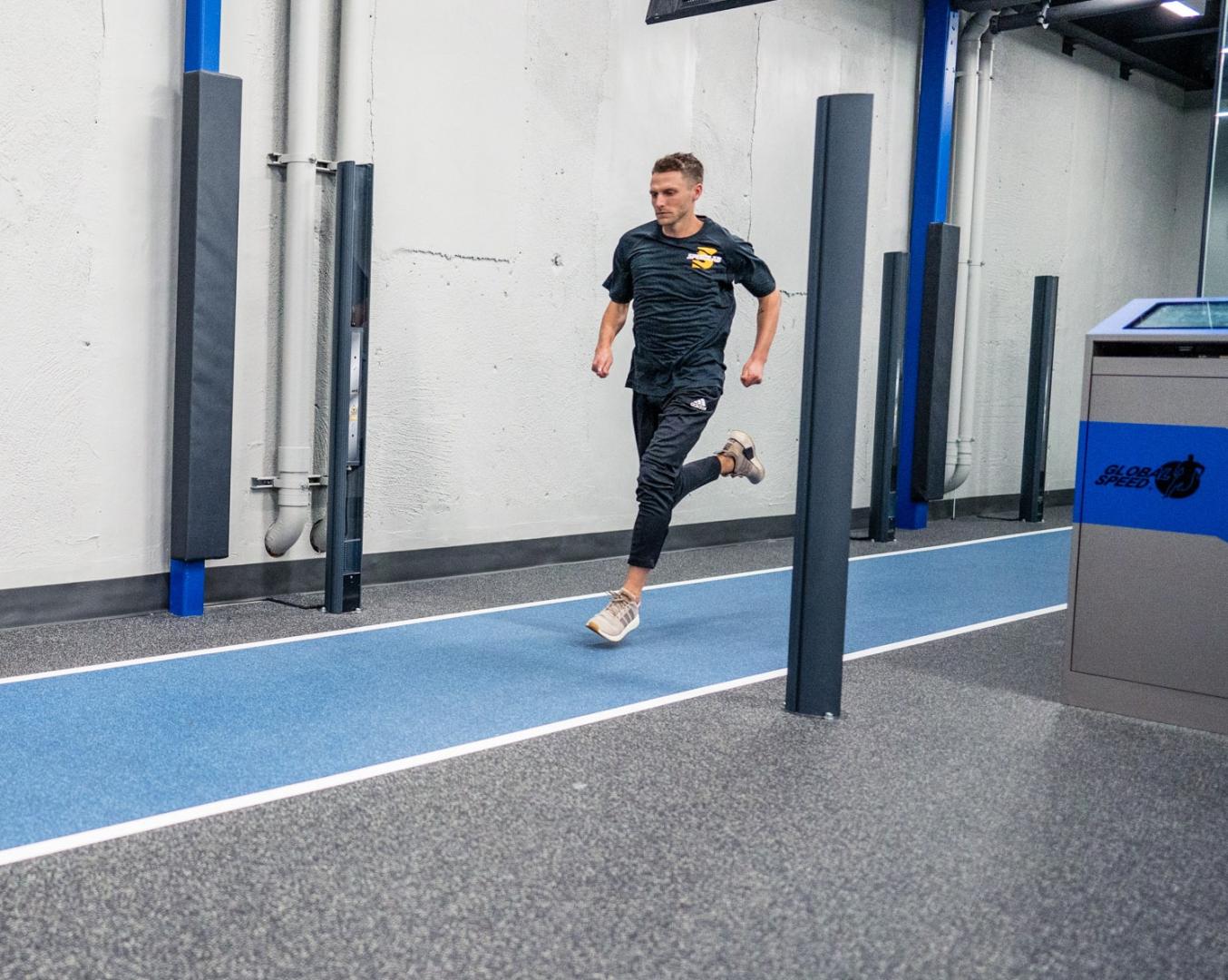 Man sprinting along a blue lane in a modern indoor gym with white walls.