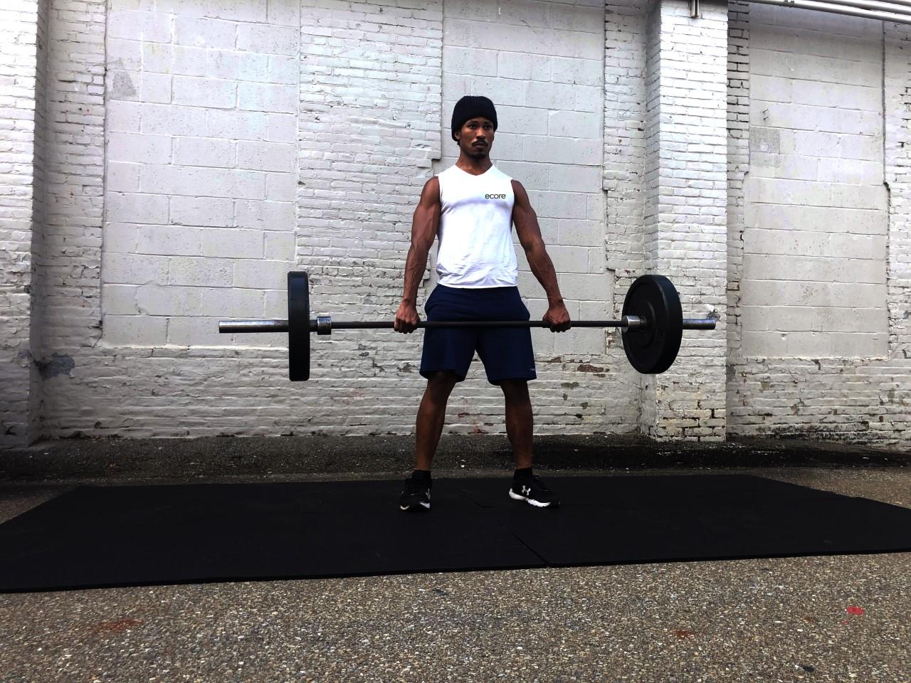 A man is positioned on a smash mat, holding a barbell in preparation for a weightlifting workout.