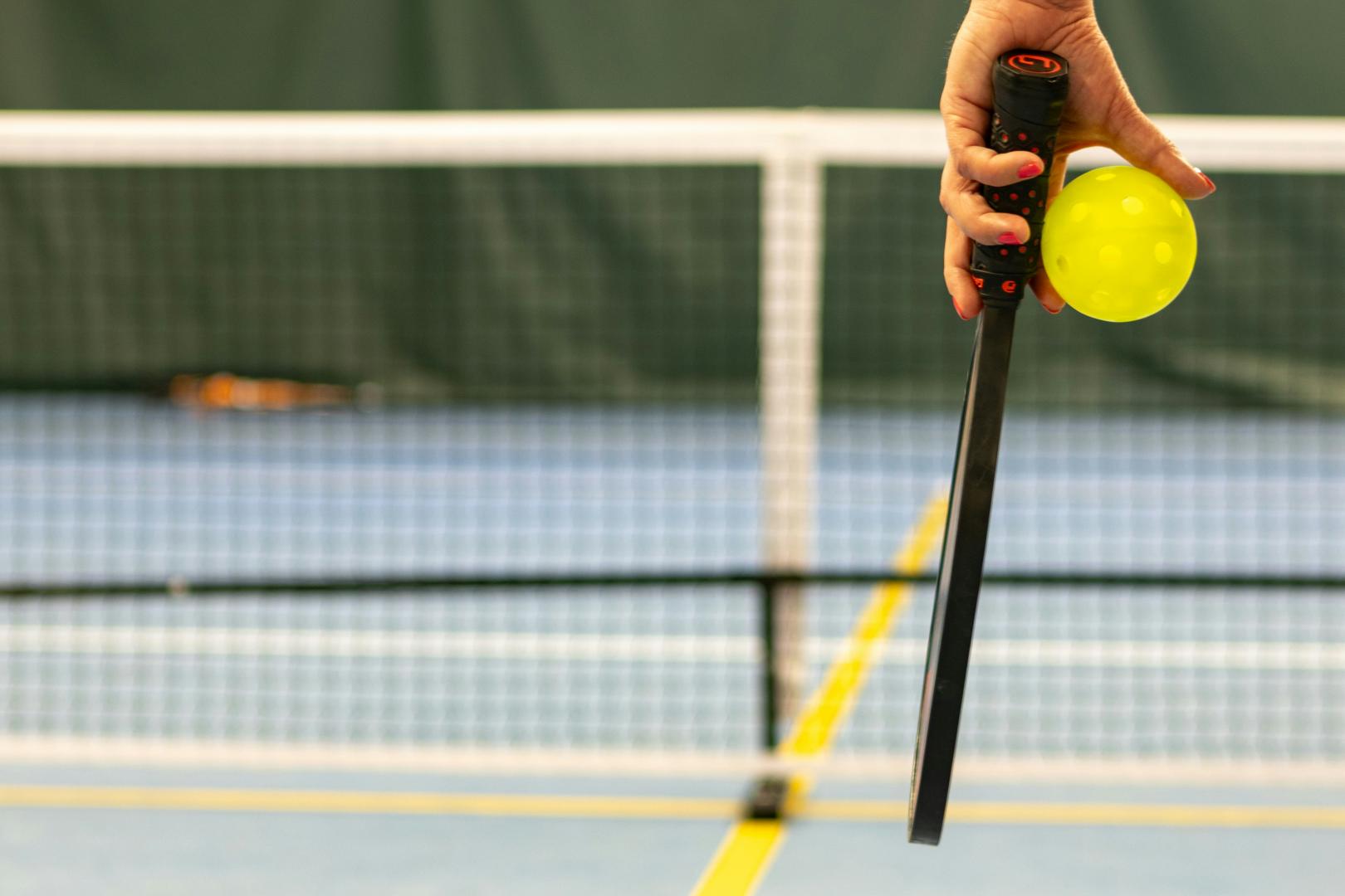 A person stands with a tennis racket in one hand and a yellow ball in the other, preparing to play.