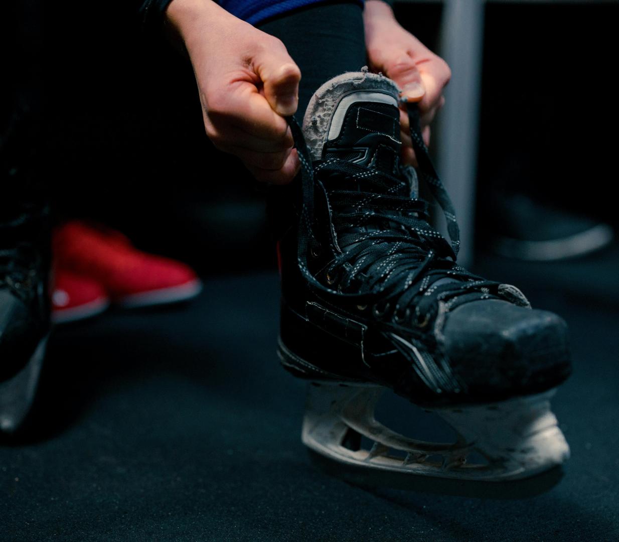 A man tying in ice skates on a Blade Ecore Athletic floor.