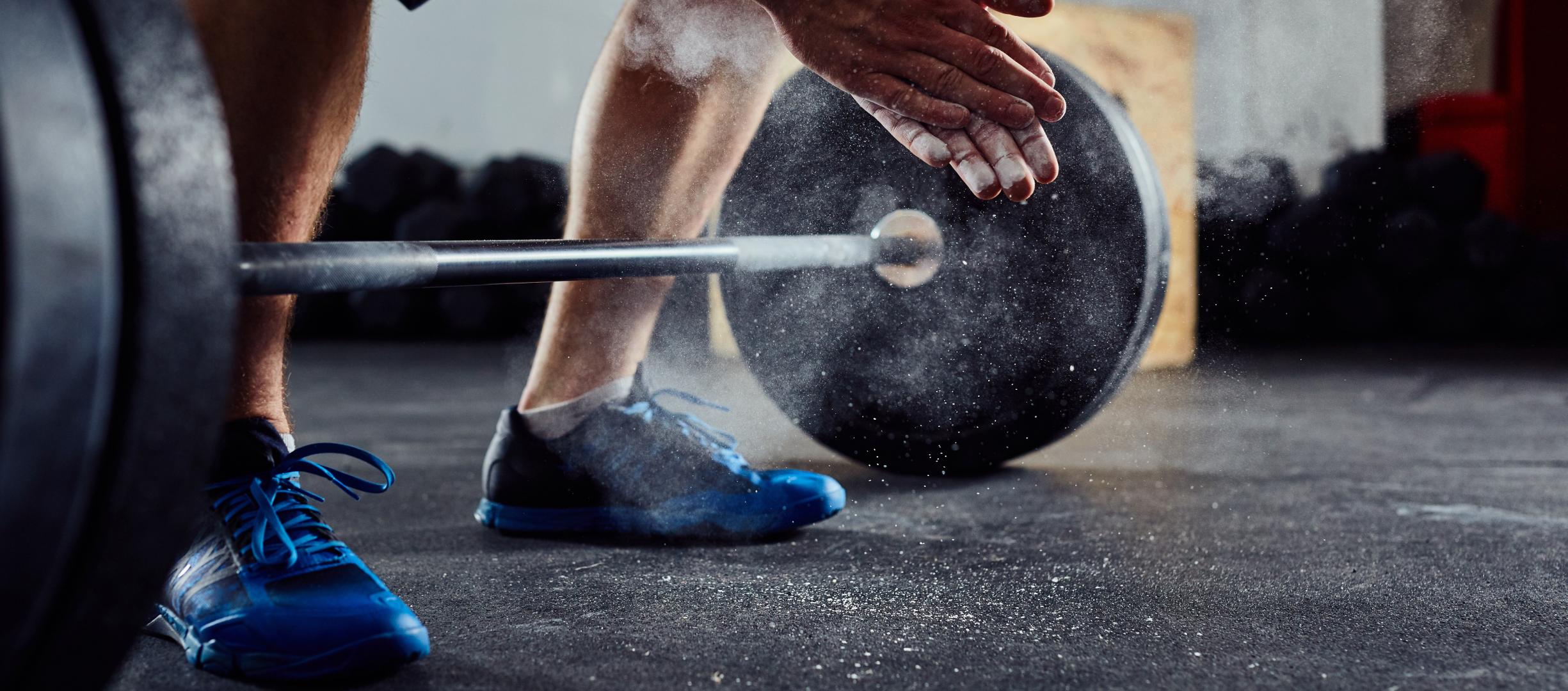 A man weightlifting about to deadlift and clapping his hands that are covered in chalk