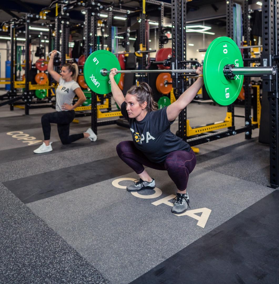 A woman doing a clean jerk with the barbell over her head in a squat