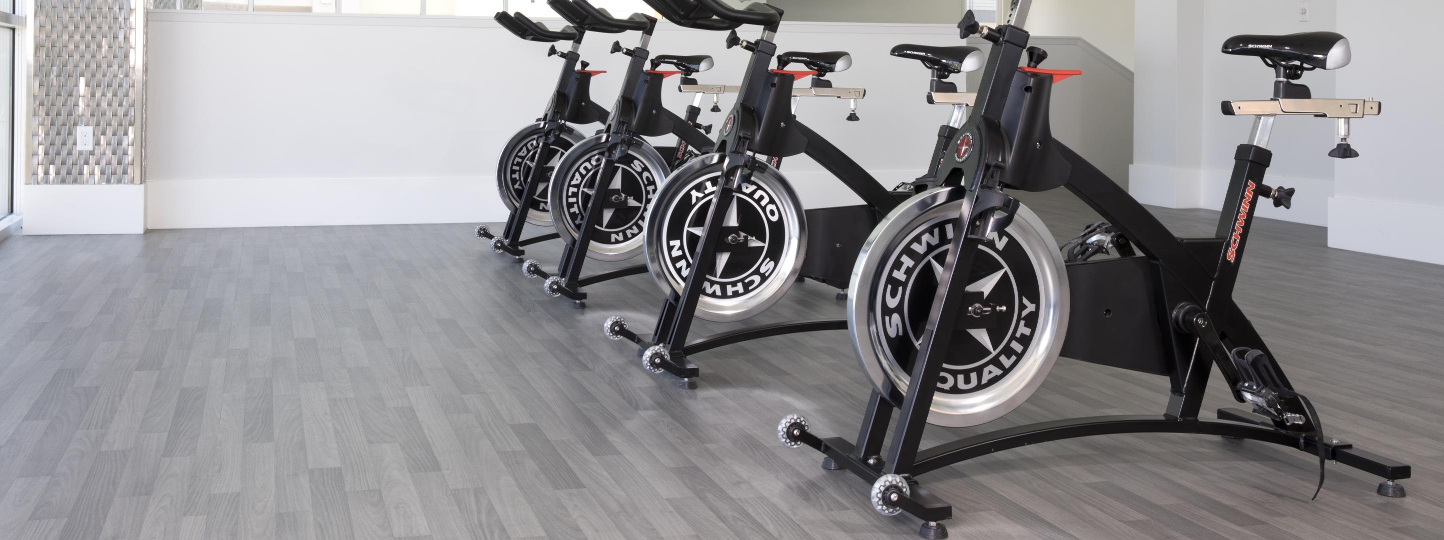 A few spin bikes in a line on a gray studio floor. 