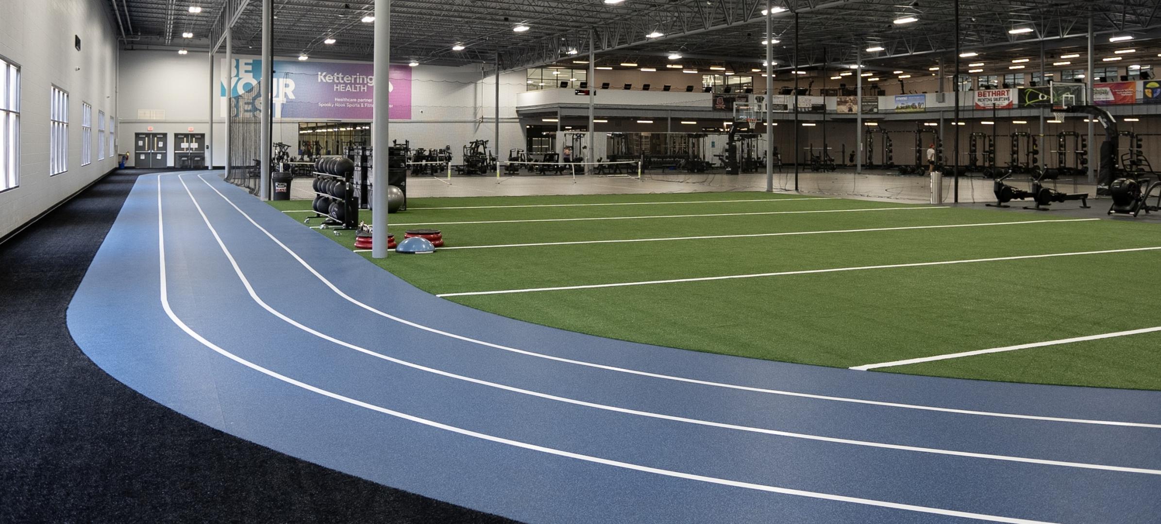 A wide shot of a large fitness facility with a running track, a turf area, and a work out area