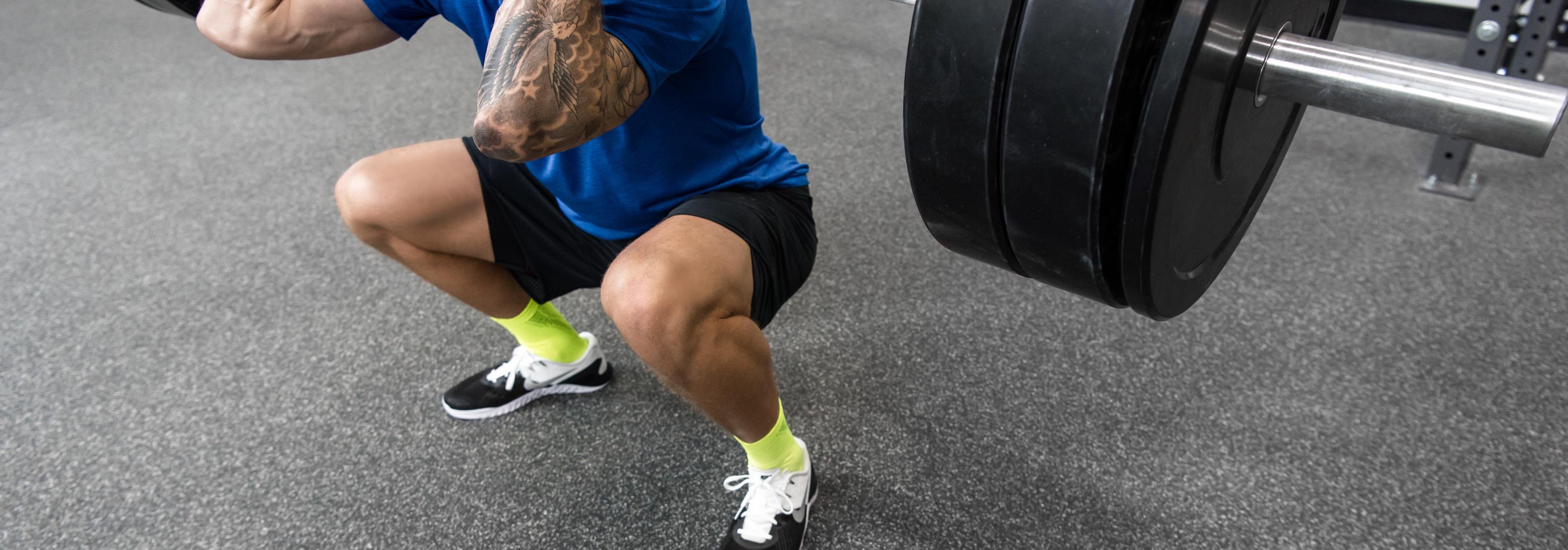 A downward angle of a man doing a squat on top of Performance flooring