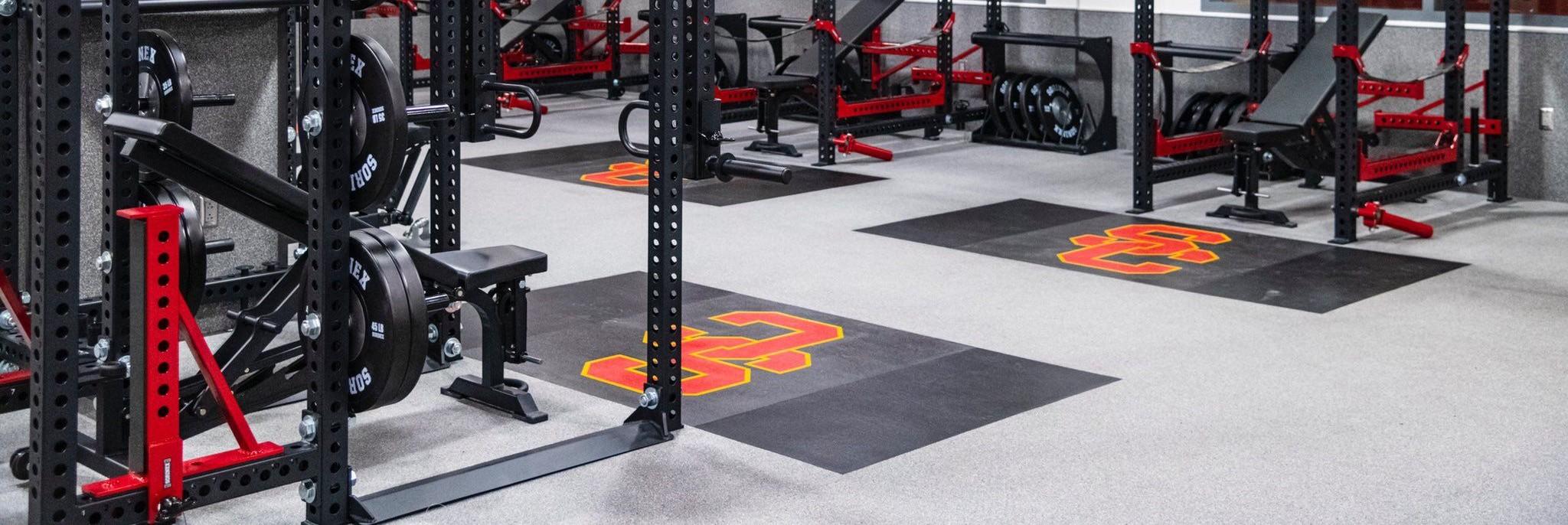 Well-equipped gym with weights and fitness equipment on a grey floor with custom logos.