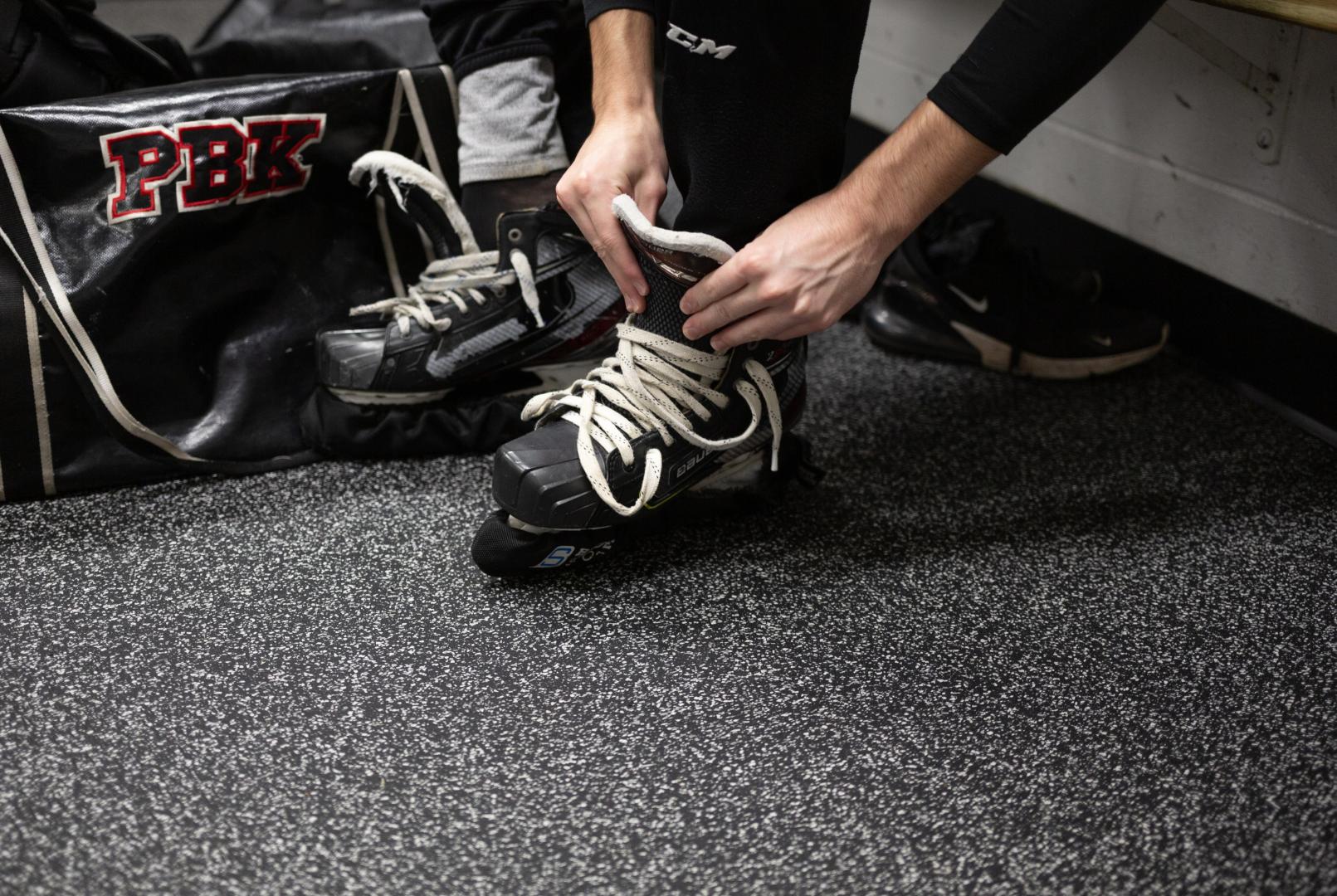 A man tying in ice skates on a Blade Ecore Athletic floor.