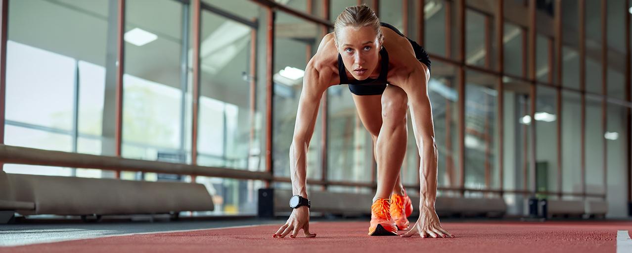 Female athlete in starting position on indoor track, focused and ready to sprint.